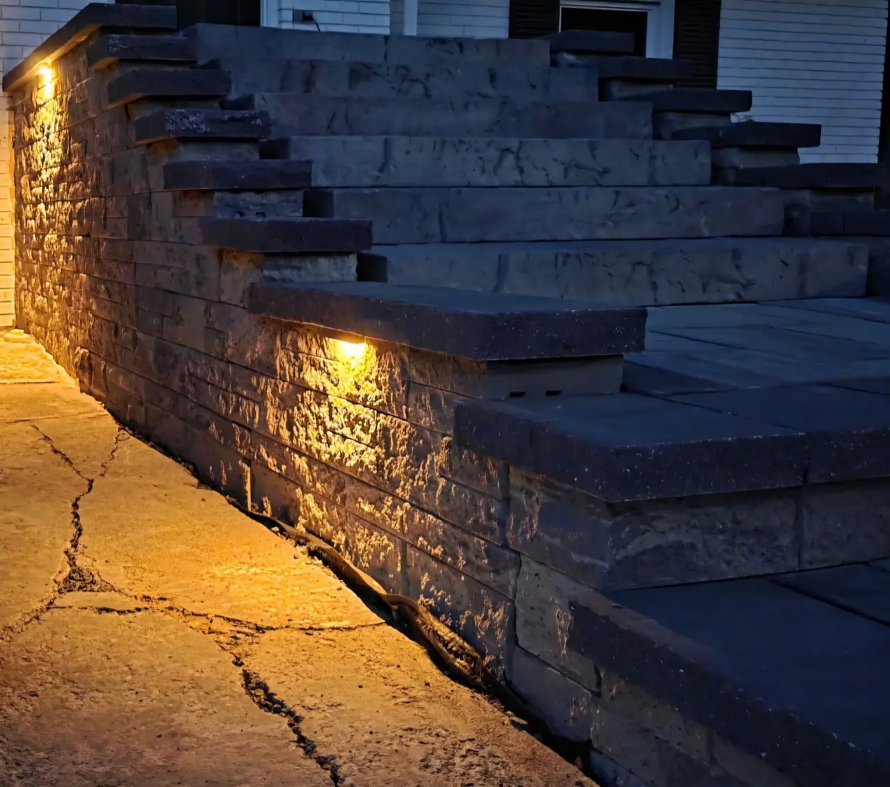 Warm lights beneath wall caps beside an outdoor stairway at dusk