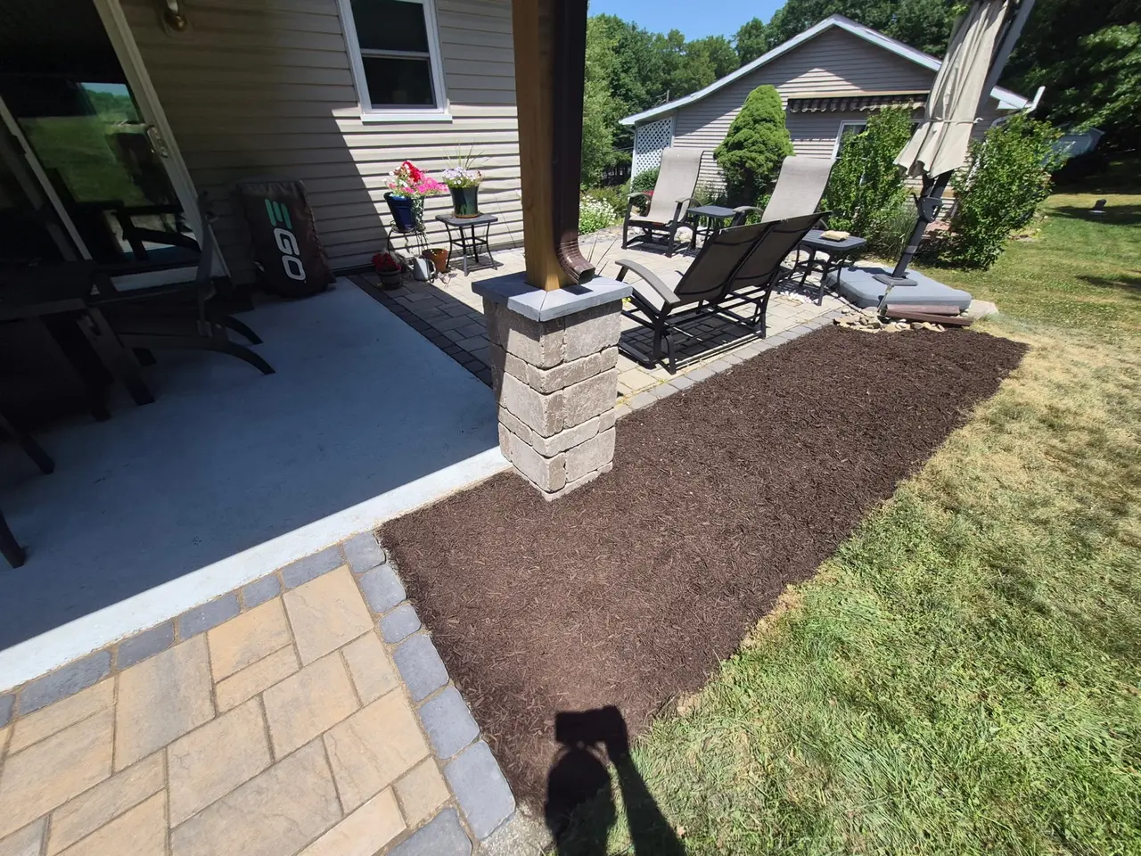 Paver seating area beside a covered porch and mulched garden bed