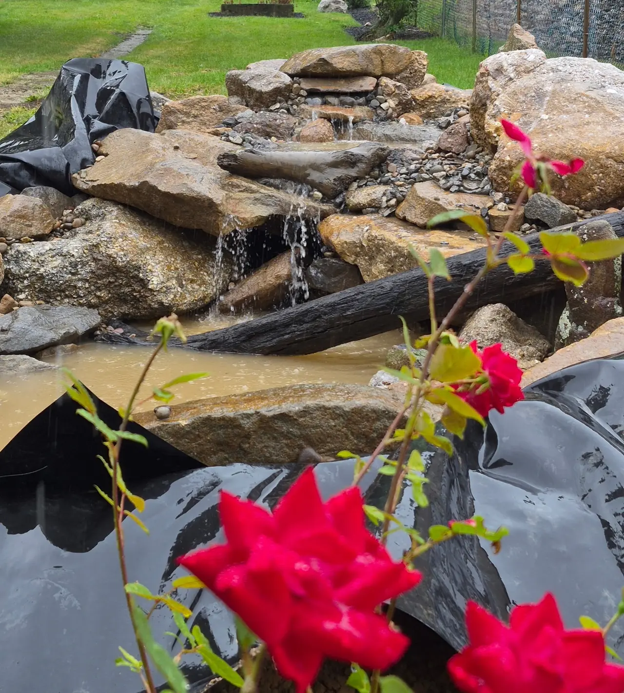 Water flowing over natural rocks with pond liner visible during construction