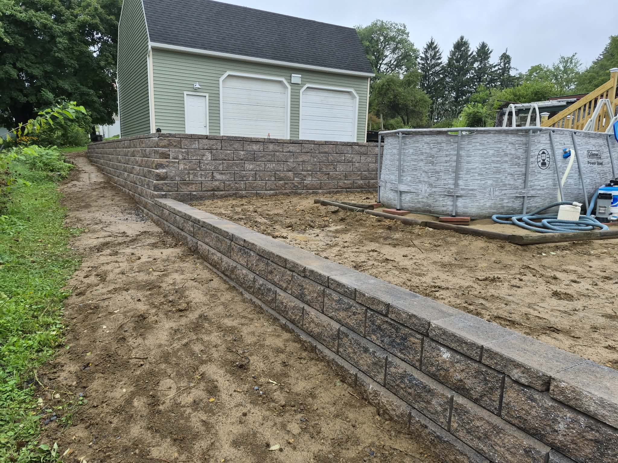 Tiered block retaining walls with capstones beside a detached garage and above-ground pool